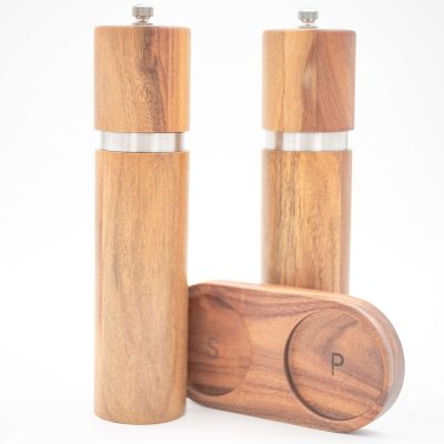 Handcrafted acacia wood salt and pepper grinders with ceramic mechanisms, displayed on a matching wooden tray with natural grain visible.
