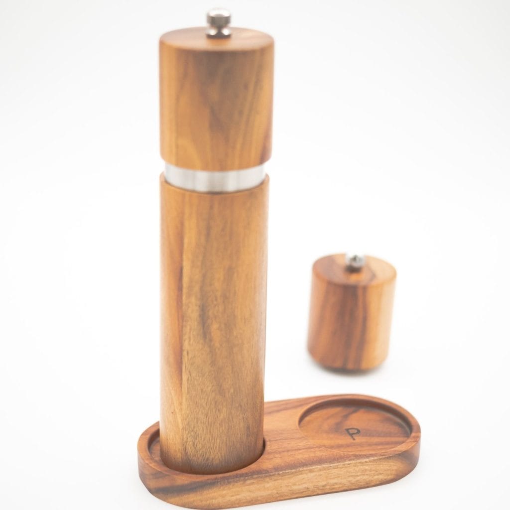 Handcrafted acacia wood salt and pepper grinders with ceramic mechanisms, displayed on a matching wooden tray with natural grain visible.